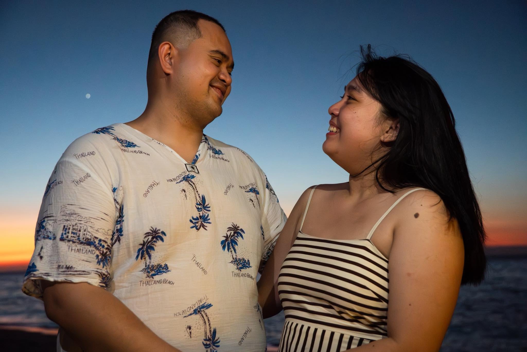A couple smiling together by the ocean at sunset