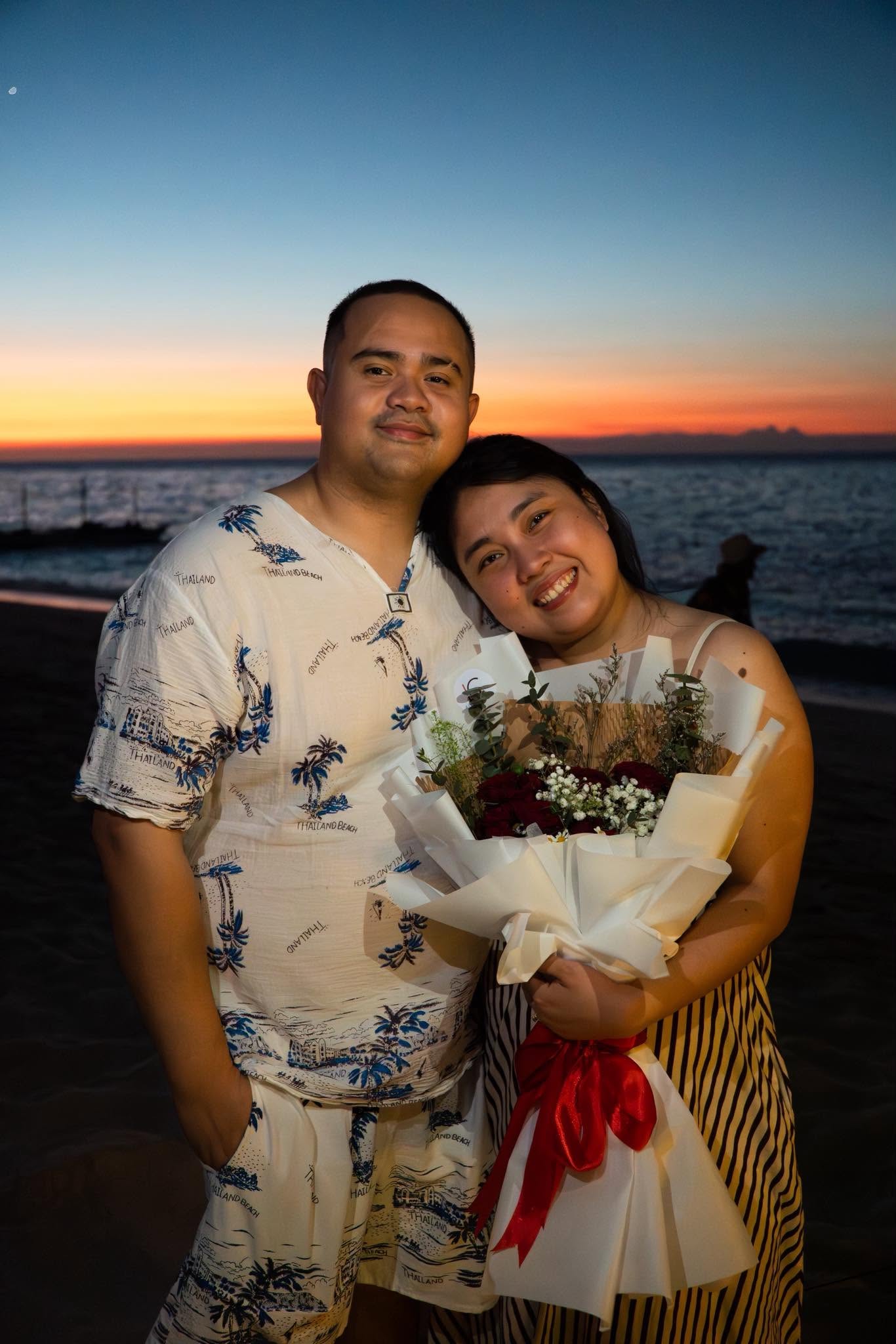 A couple embracing with flowers by the ocean at sunset